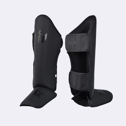 Pair of black GSX Gladiator martial arts shin guards with a Spartan helmet logo, shown from the front and back.